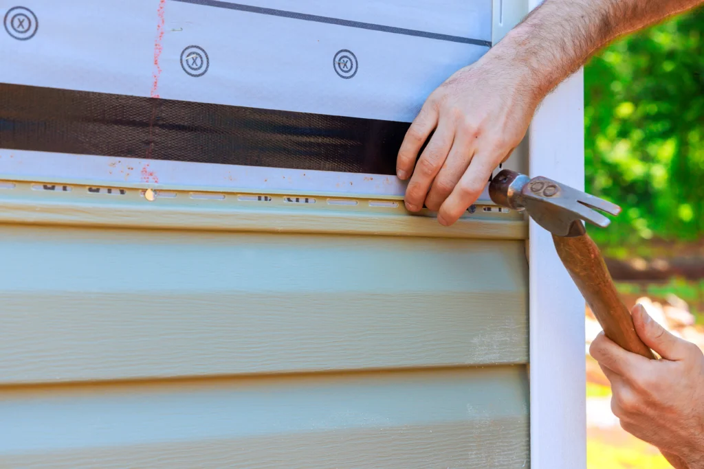 Worker using a hammer to help install new vinyl siding on a building